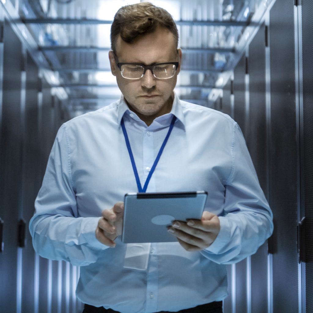 a man walking down a server room holding a tablet